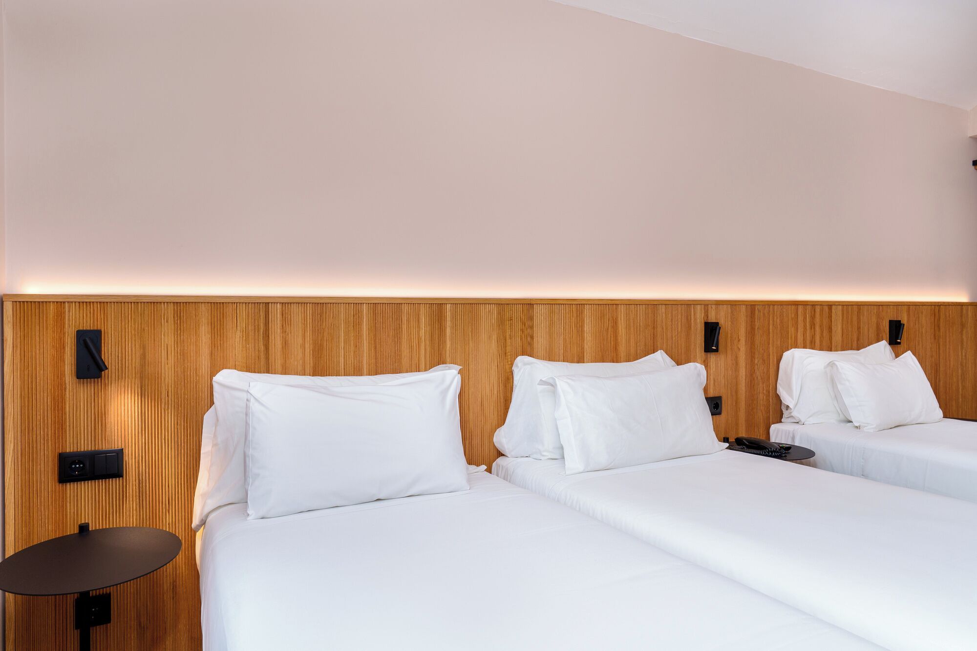 Habitación de hotel con dos camas, cabecero de madera, una mesita y teléfono en la pared.