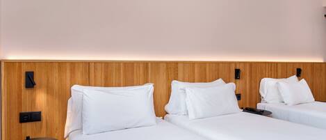 Habitación de hotel con dos camas, cabecero de madera, una mesita y teléfono en la pared.