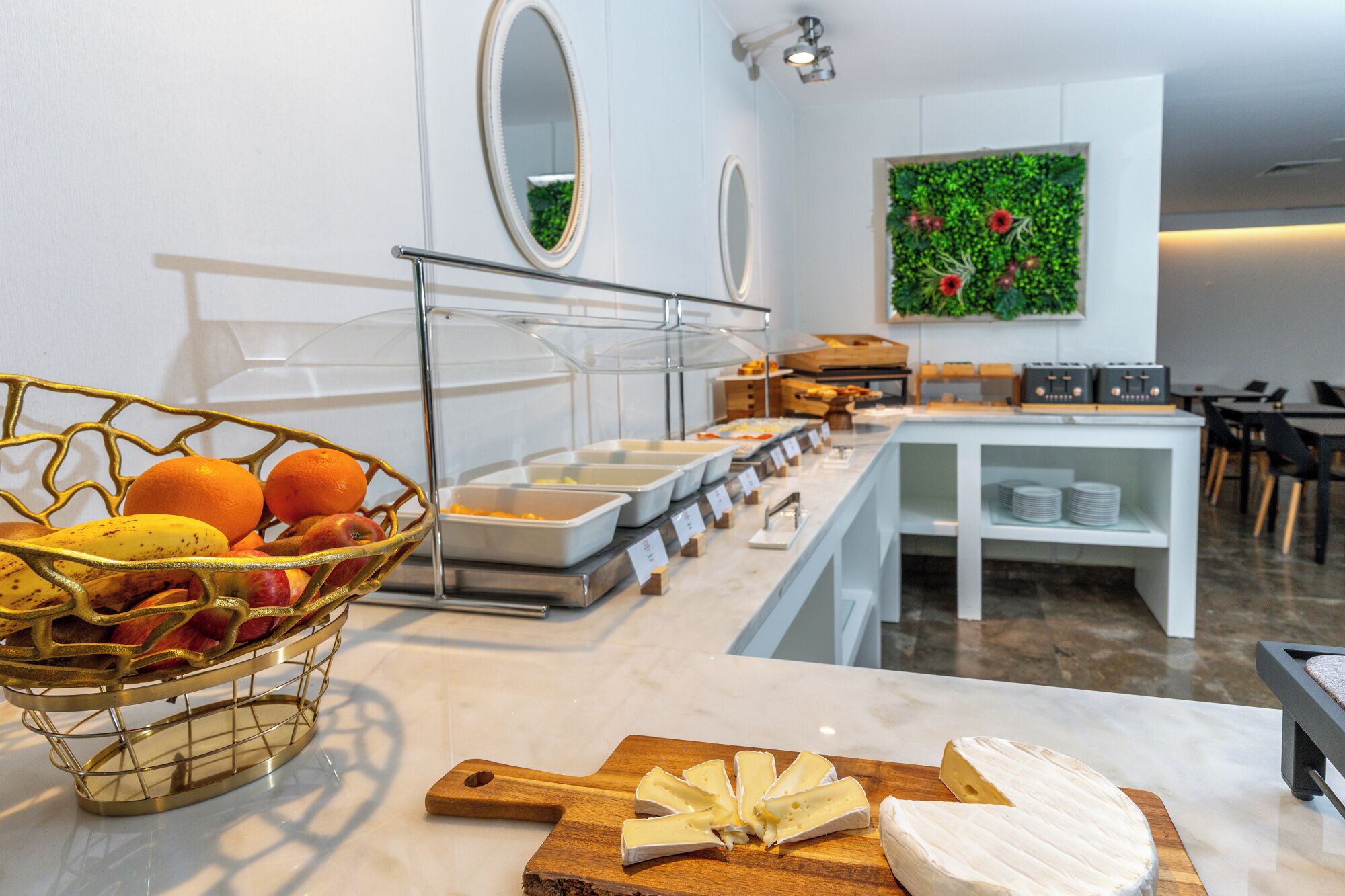 A buffet setup with a variety of food items, a cheese board, and a decorative wall.