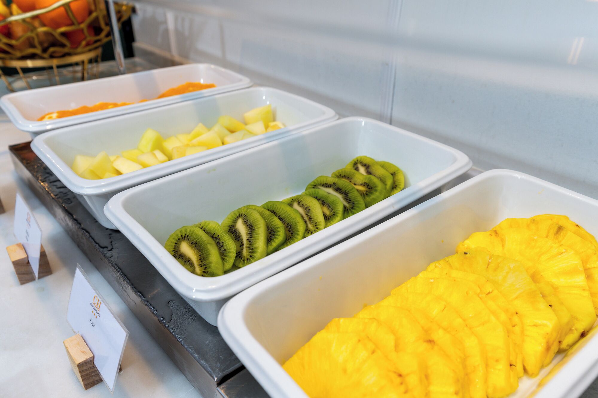 Un bufé con opciones de fruta, incluyendo piña, kiwi y mango.