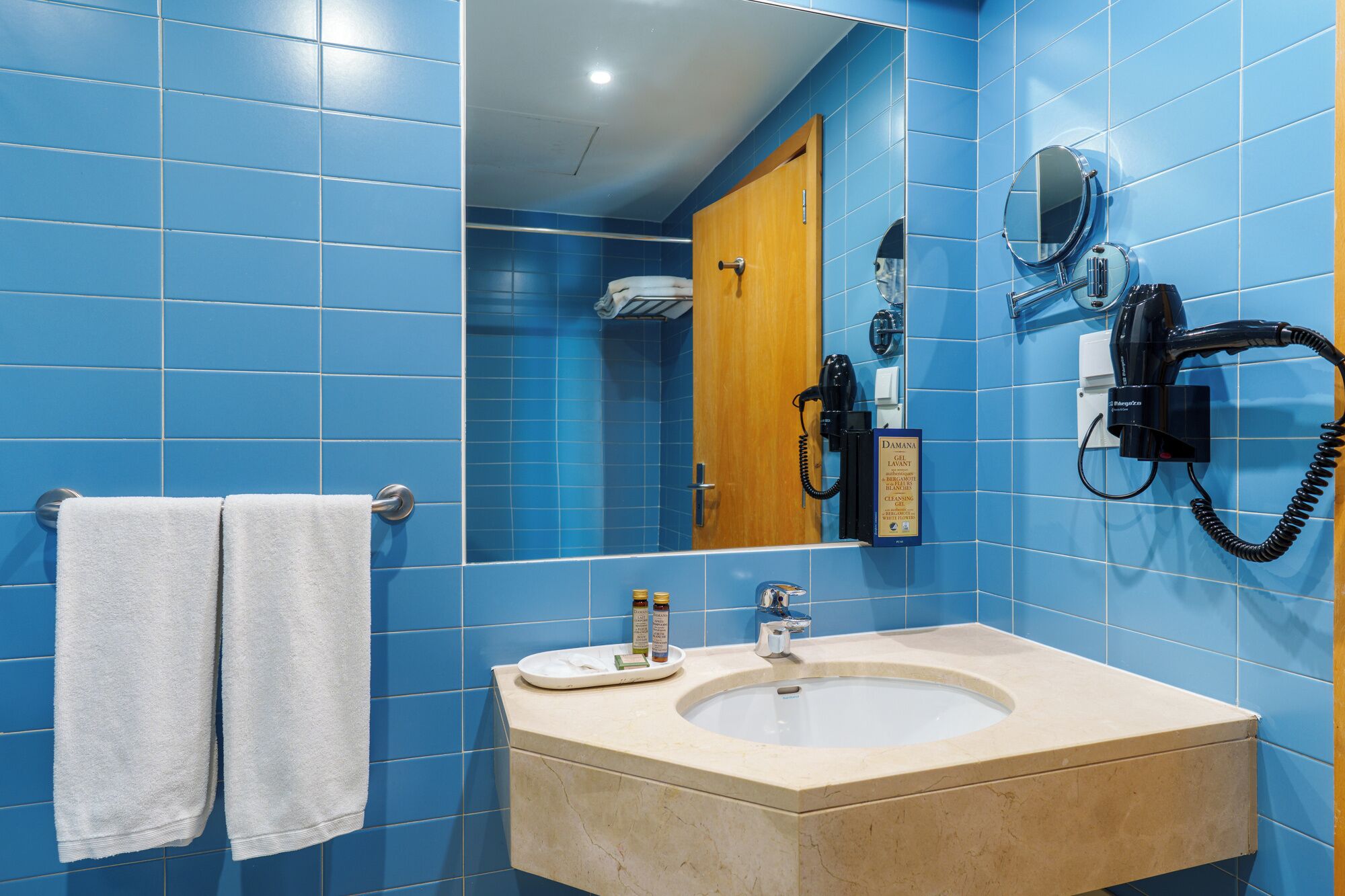 A bathroom with blue tiles, a sink, a mirror, a towel rack, and a hairdryer.