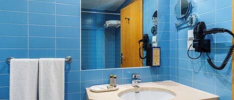 A bathroom with blue tiles, a sink, a mirror, a towel rack, and a hairdryer.