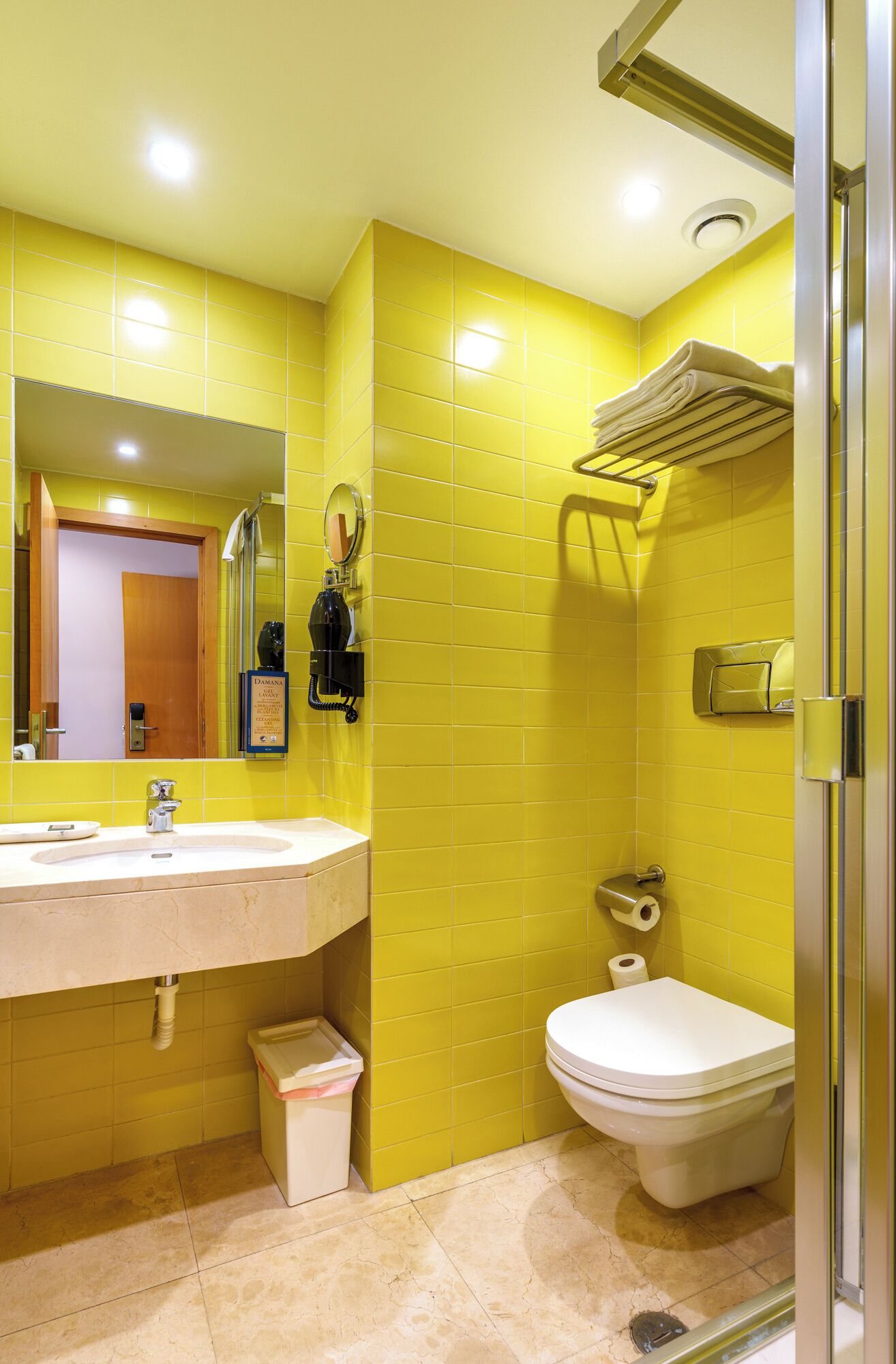 Ein Badezimmer mit gelben Wänden, einem Waschbecken inklusive Spiegel, einer Toilette und einer Duschkabine.