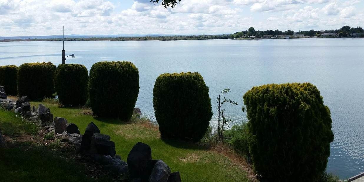 A calm lake with neatly trimmed hedges and a stone wall in the foreground.