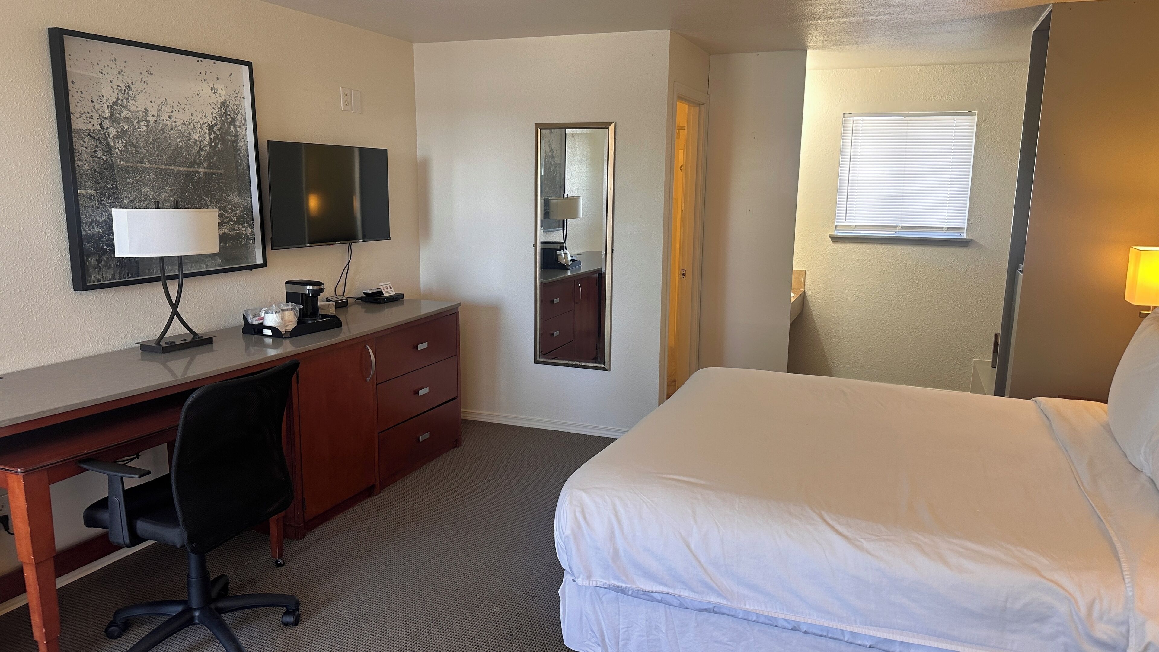 A hotel room with a desk, chair, bed, and a mirror.