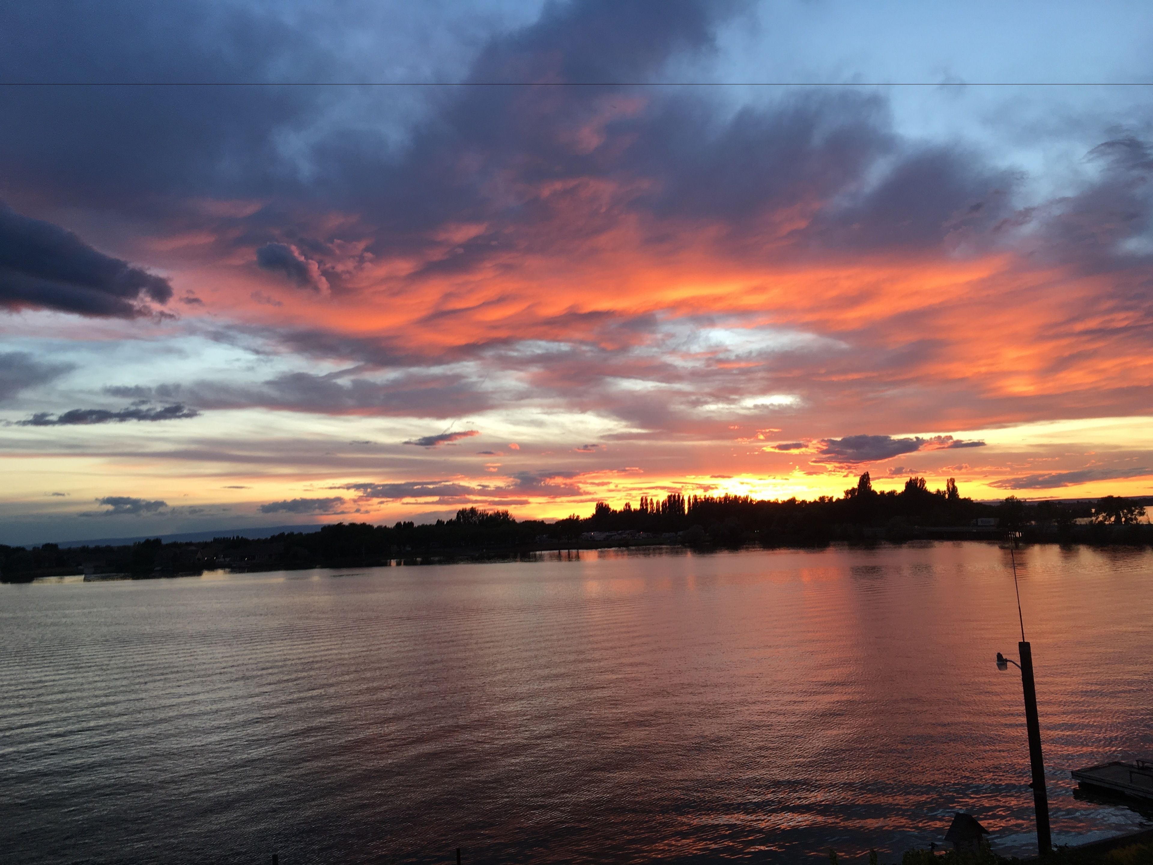 Un atardecer sobre un lago tranquilo con el perfil de un pueblo a lo lejos.