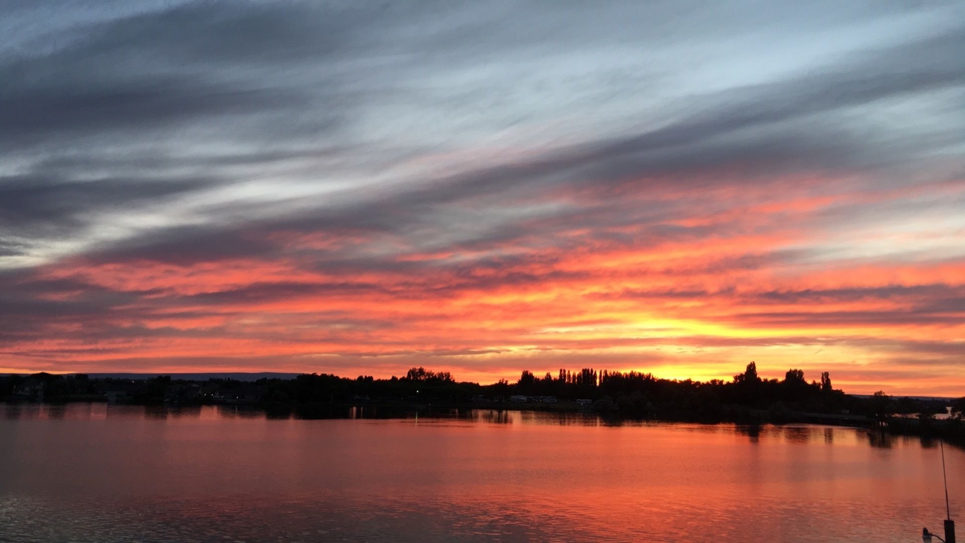 Ein Sonnenuntergang über einem stillen See, im Hintergrund die Silhouette einer Stadt.