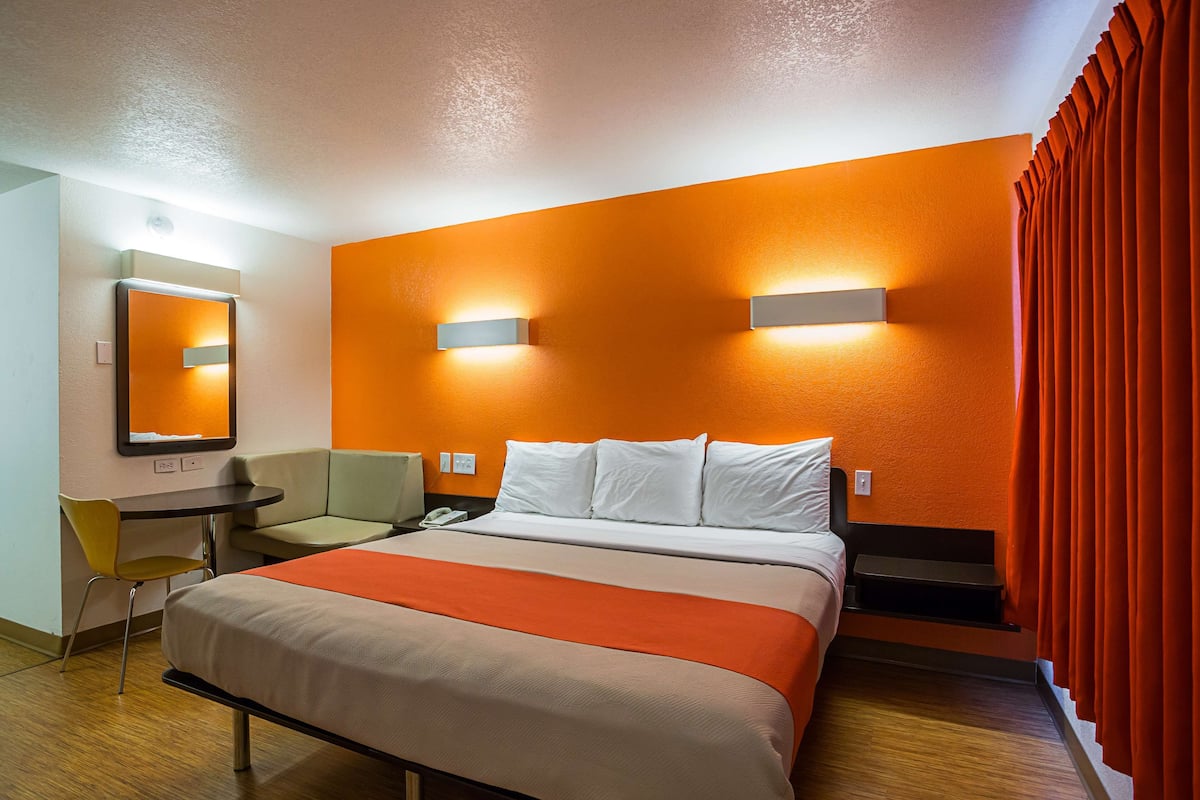 A hotel room with a bed, a desk, a chair, and a mirror.