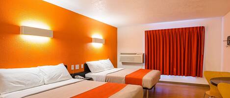 Une chambre d’hôtel avec deux lits, un bureau, une chaise et une fenêtre avec des rideaux rouges.