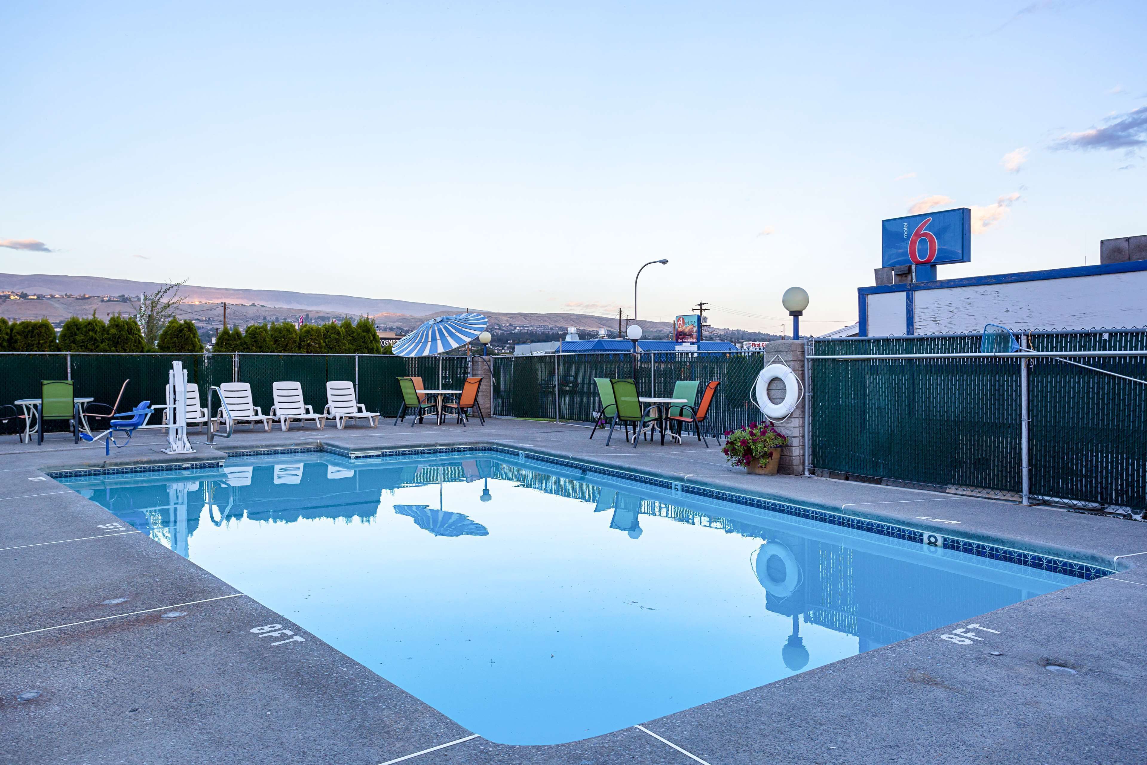 A swimming pool with lounge chairs and umbrellas, surrounded by a fence and a view of hills.
