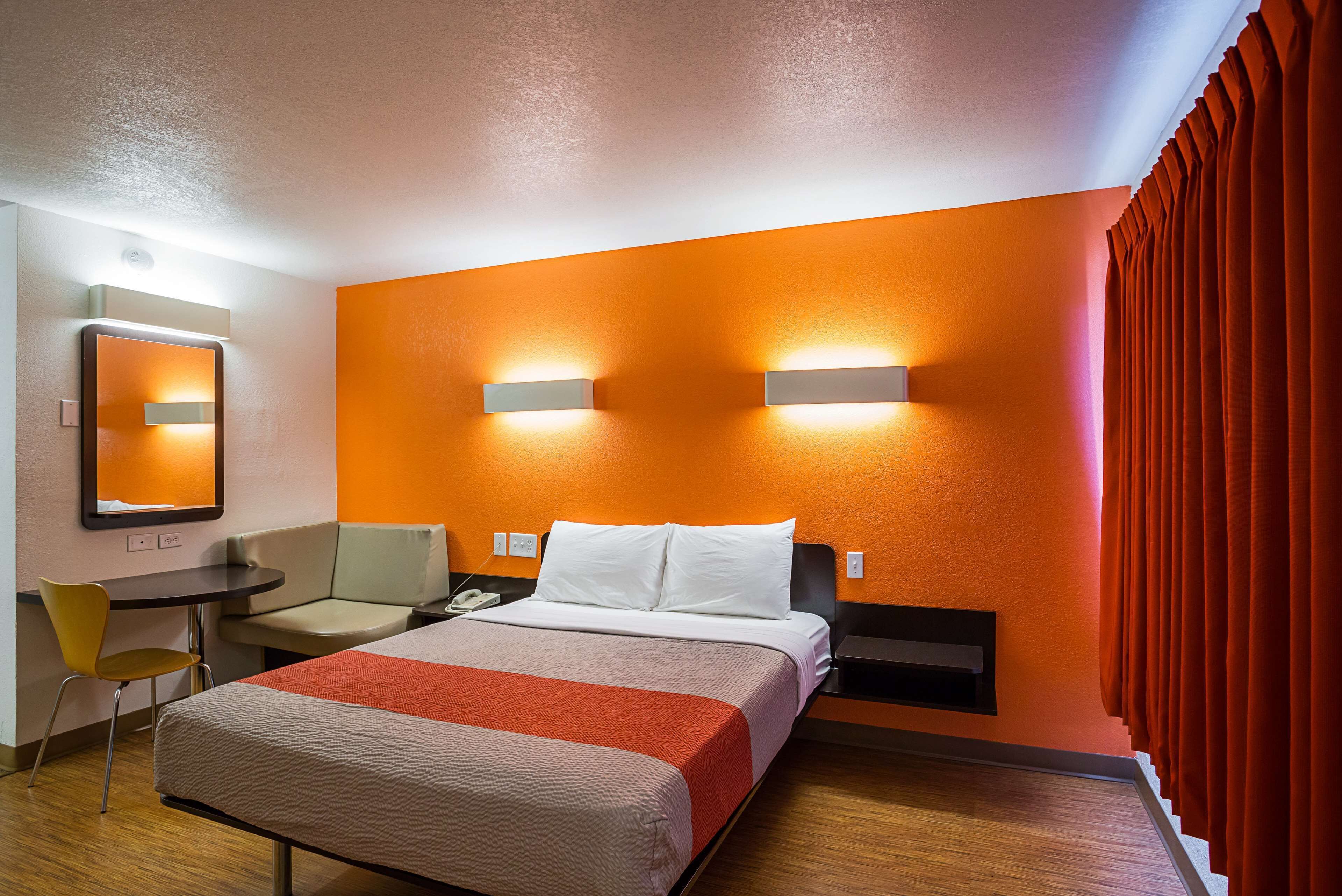 A hotel room with a bed, a desk, a chair, and a mirror.