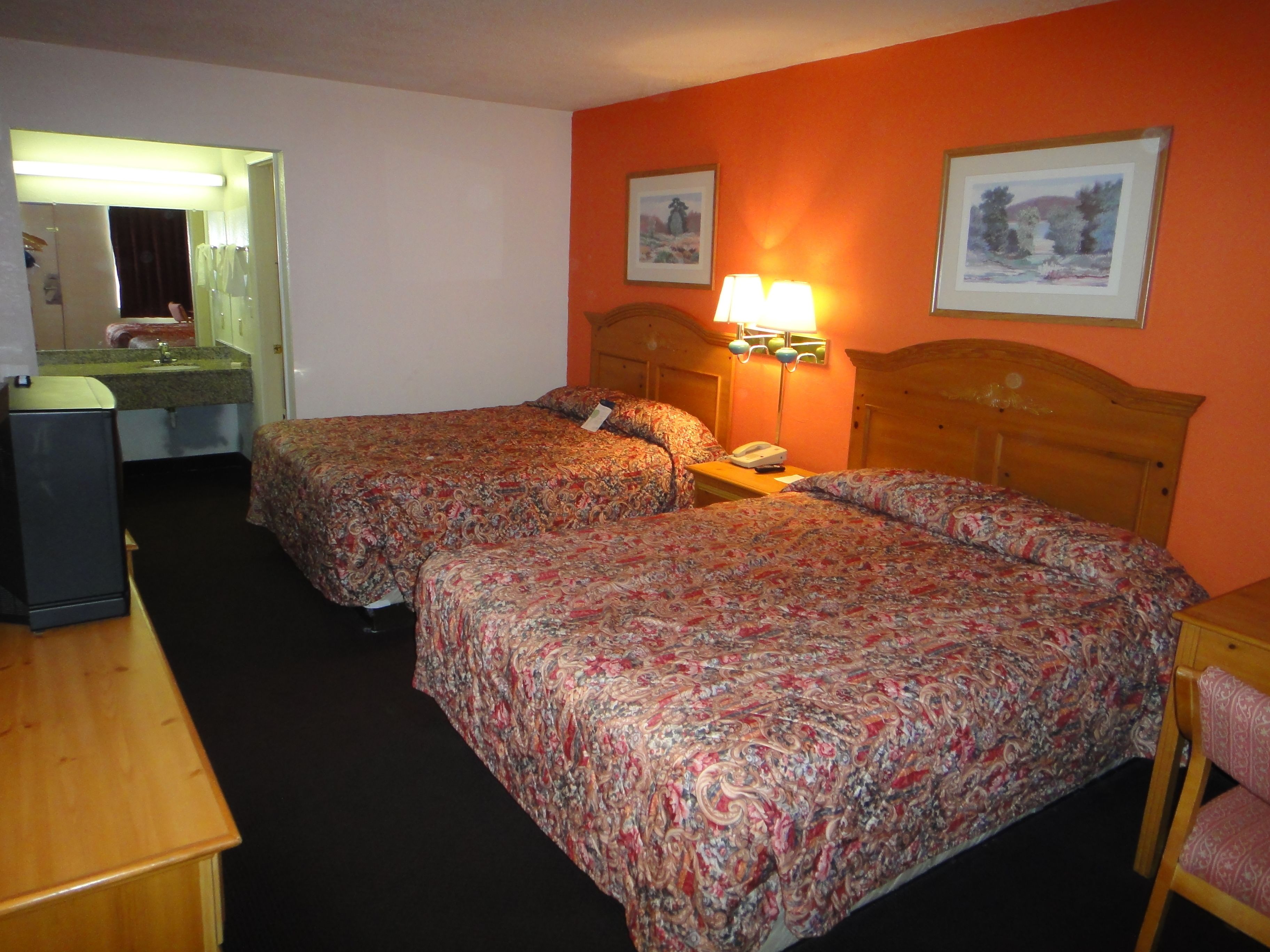 A hotel room with two beds, a desk, a mirror, and a bathroom visible through an open door.