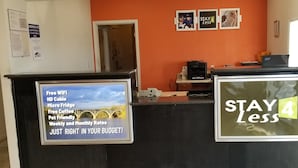 A hotel reception area with a signboard listing amenities like free WiFi, HD cable, micro fridge, free coffee, and pet-friendly services. - Stay 4 Less (Fredericksburg)