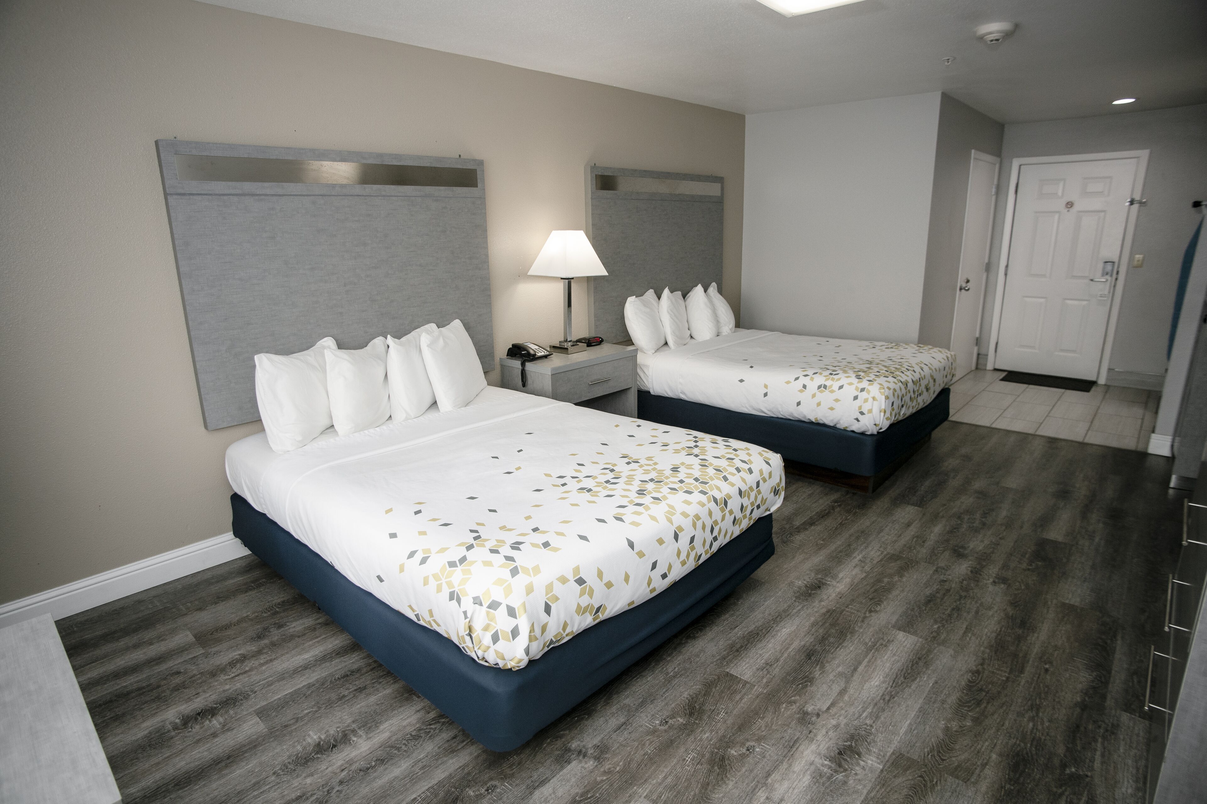 A hotel room with two beds, a nightstand with a lamp, and a door.