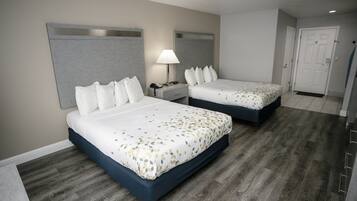 A hotel room with two beds, a nightstand with a lamp, and a door.