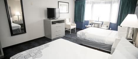 A hotel room with a large bed, a TV on a dresser, a desk with a chair, and a window with curtains.