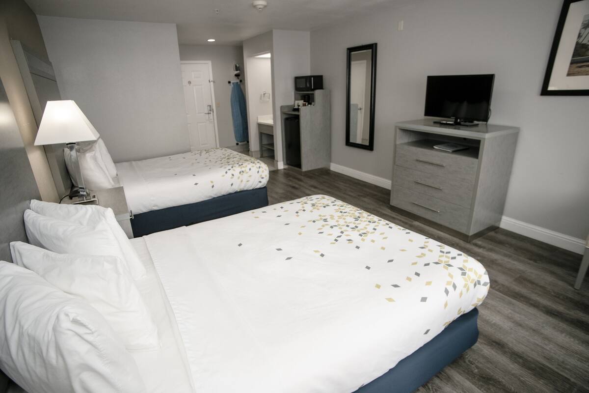A hotel room with two beds, a desk, a television, and a bathroom visible through an open door.