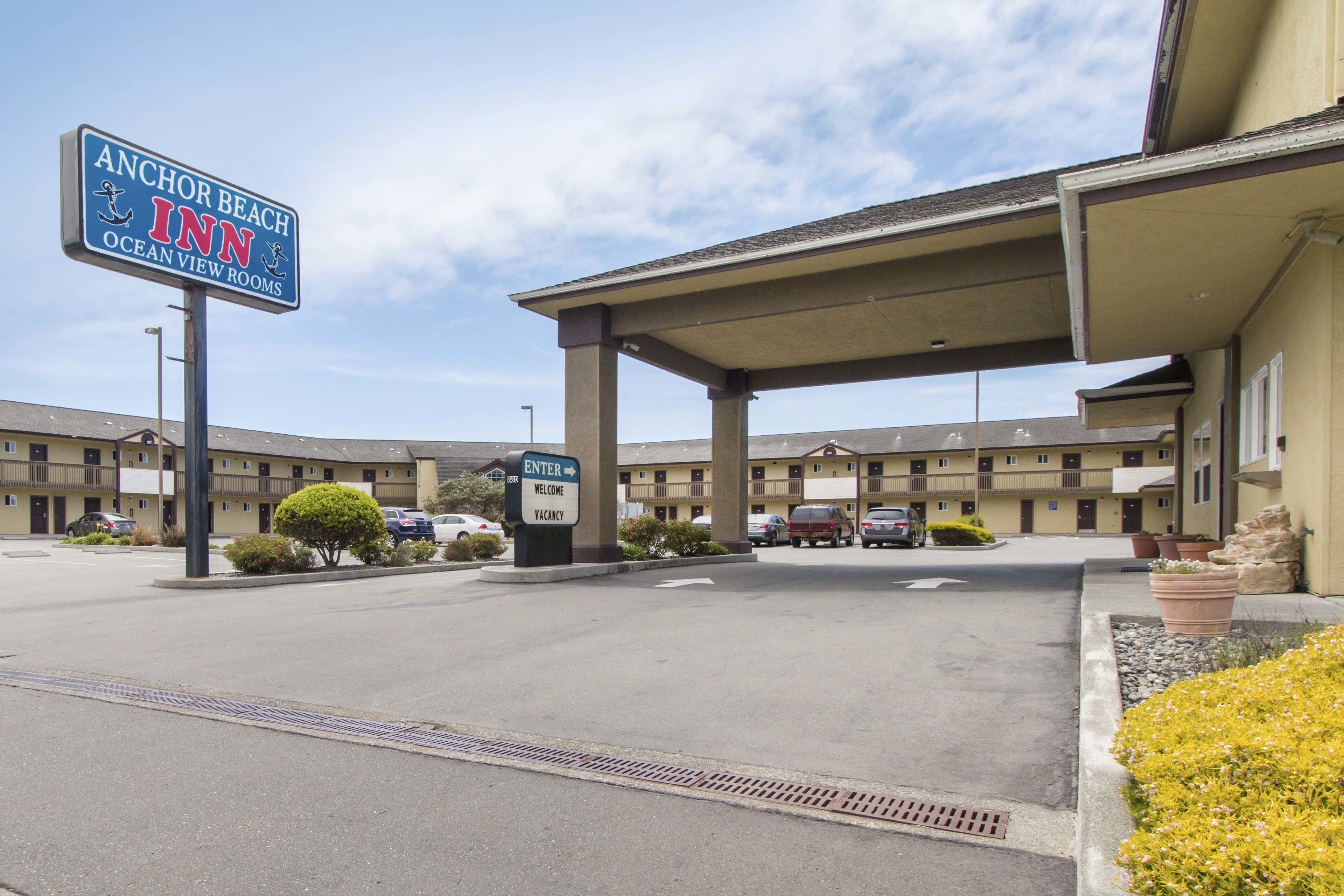 A motel named Anchor Beach Inn with Ocean View Rooms, featuring a covered parking area and a building with multiple balconies.