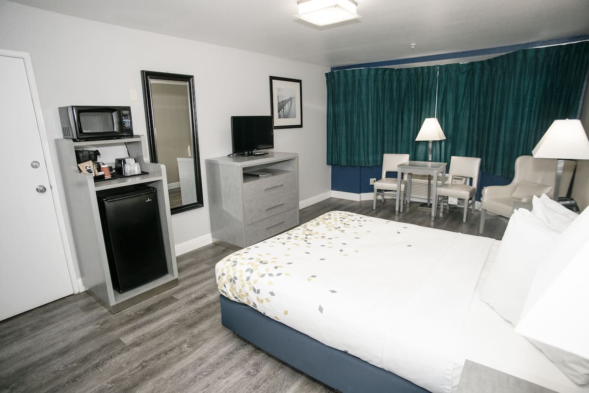 A hotel room with a bed, a desk, a chair, a television, a microwave, and a refrigerator.