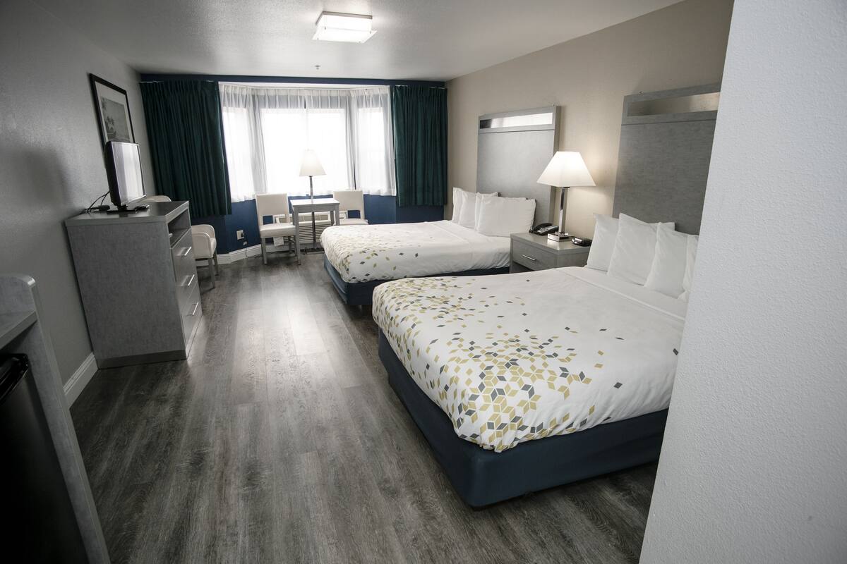 A hotel room with two beds, a desk, a chair, a desk lamp, a telephone, and a television.