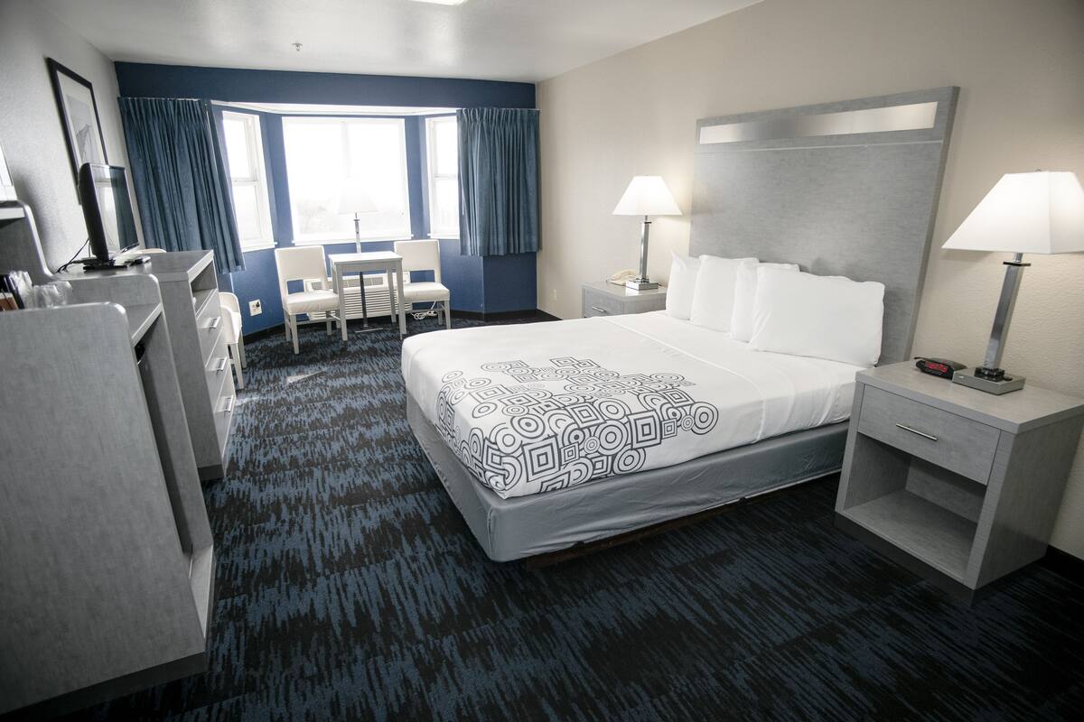 A hotel room with a large bed, two bedside tables with lamps, a desk with a chair, a TV, and a window with curtains.