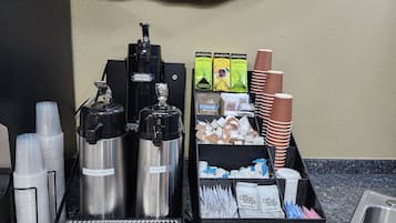 A coffee station with two hot water dispensers, a variety of coffee pods, disposable cups, and a sink.