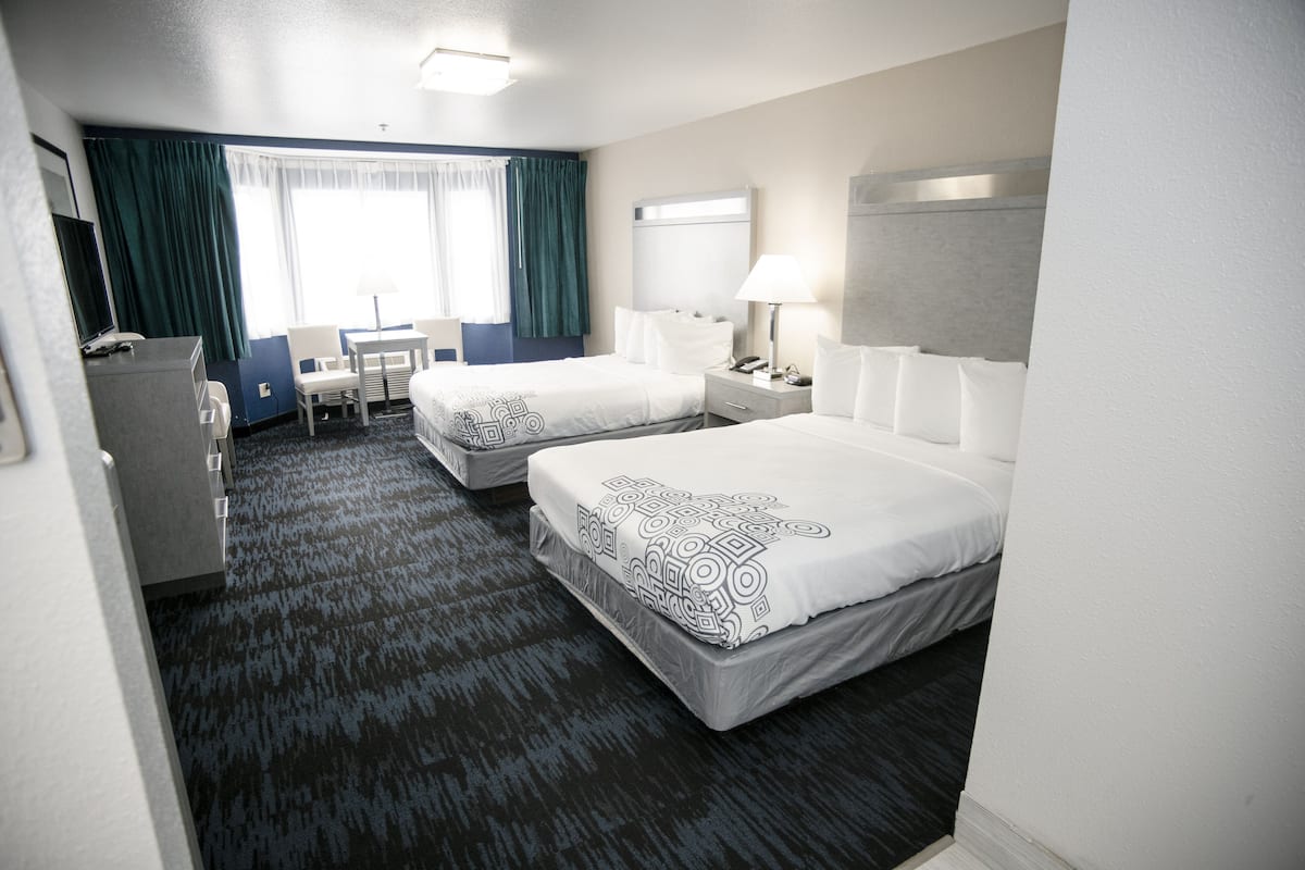 A hotel room with two beds, a desk, a chair, a TV, and a window with curtains.