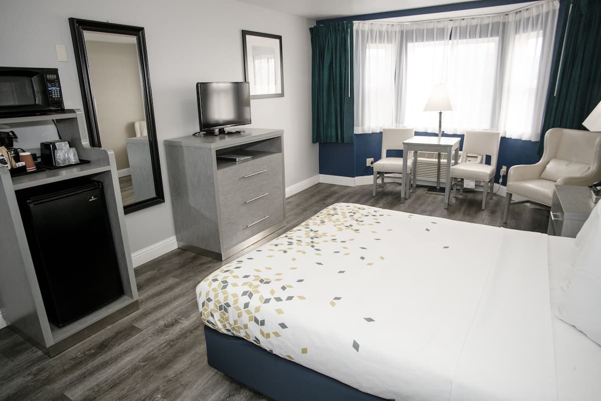 A hotel room with a bed, a desk, a chair, a television, a refrigerator, and a mirror.