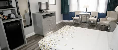 A hotel room with a bed, a desk, a chair, a television, a refrigerator, and a mirror.