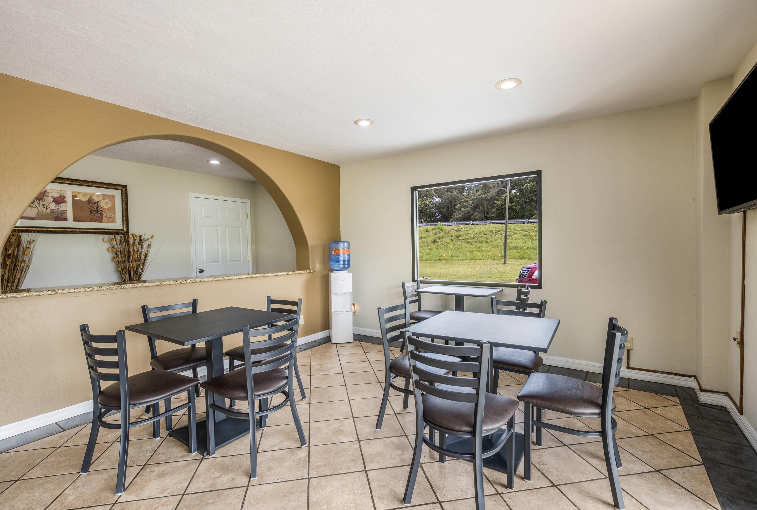 A dining area with tables and chairs, a water cooler, a door, and a window with a view of a grassy area.