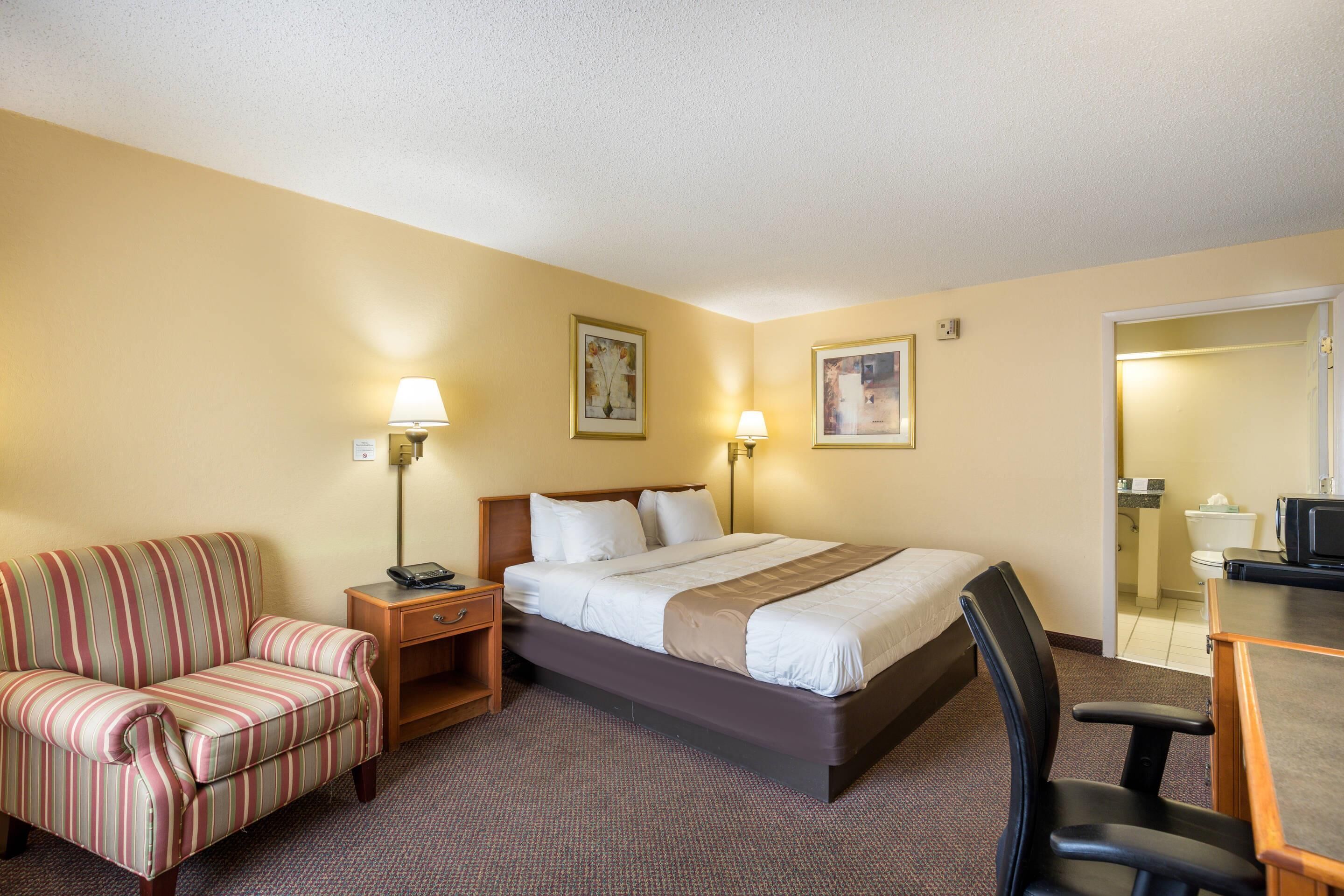 A hotel room with a bed, a striped sofa, a desk, and a chair.