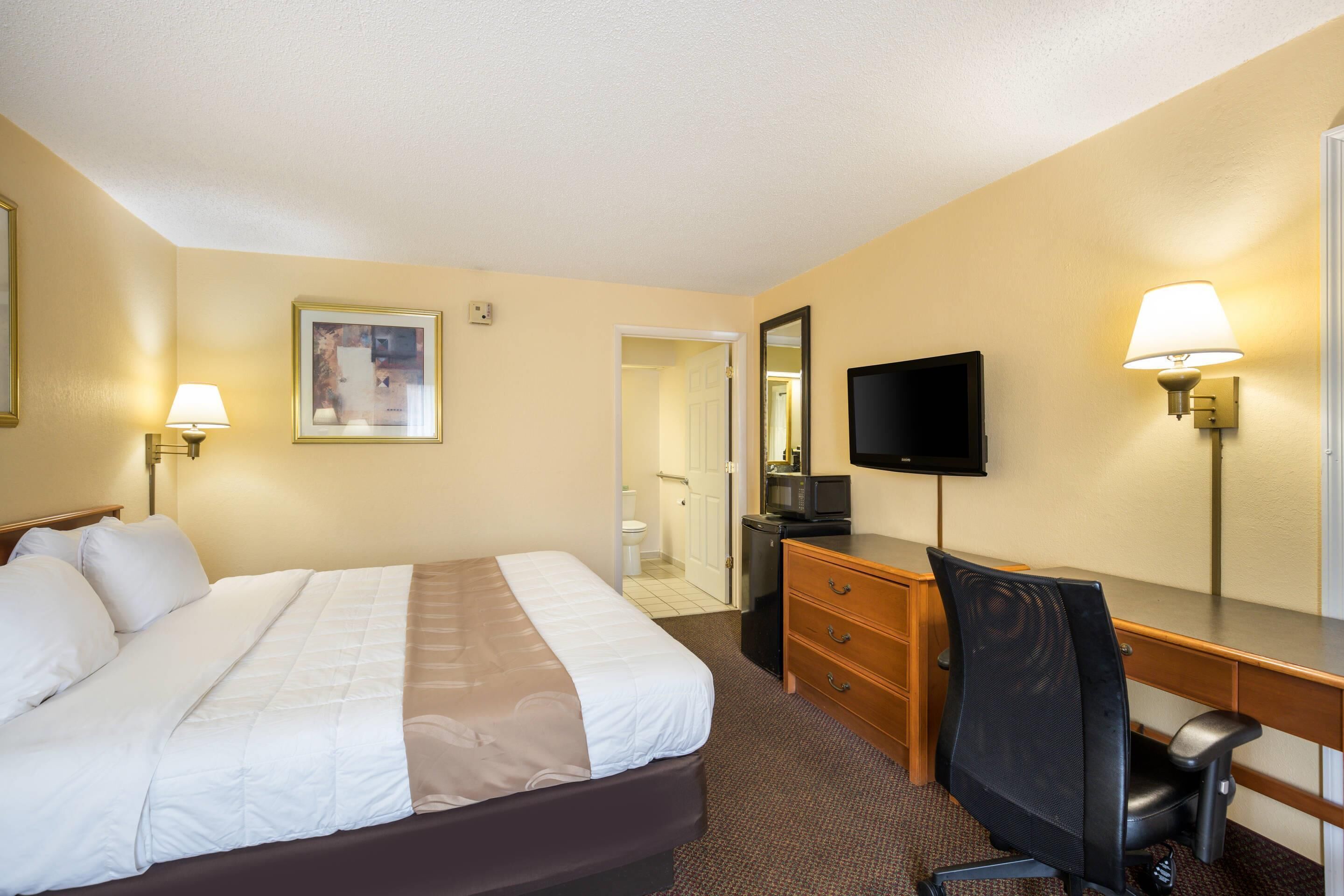 A hotel room with a bed, desk, chair, television, and a bathroom door.