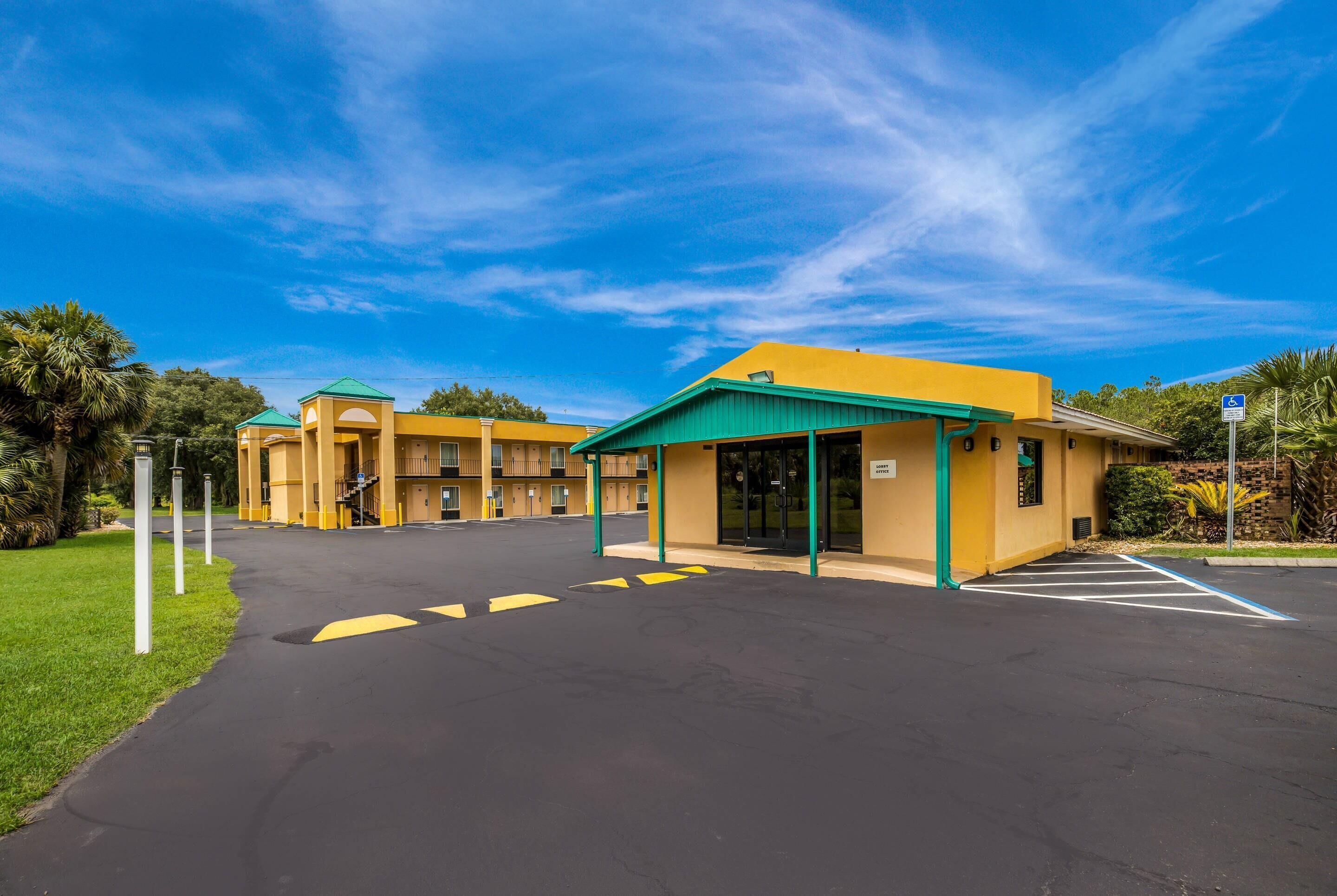 A hotel with a green roof, yellow walls, and a parking lot with marked spaces.