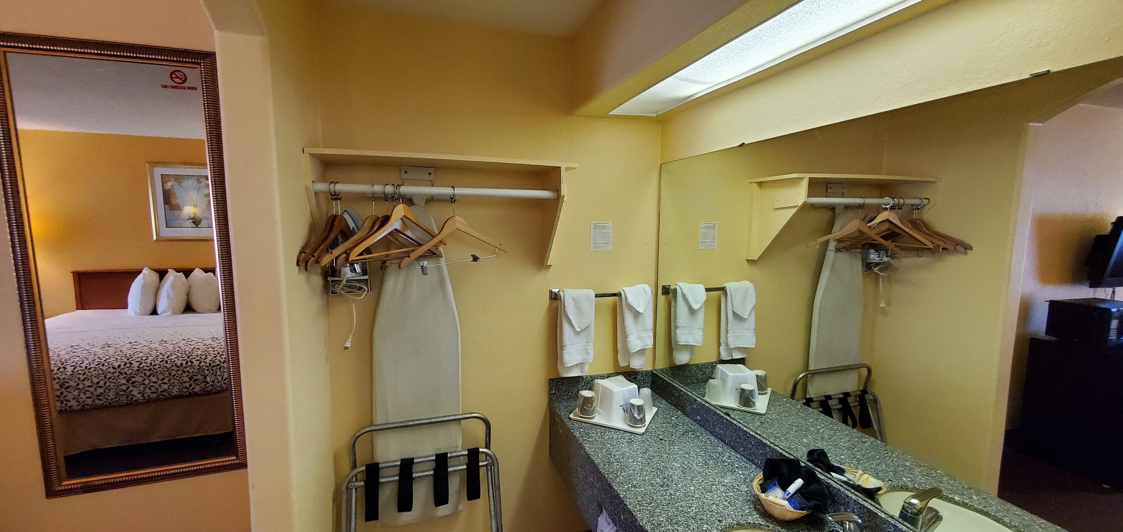 Une salle de bain d’hôtel équipée d’un lit, d’un porte-serviettes, d’un miroir, d’un lavabo et d’articles de toilette.
