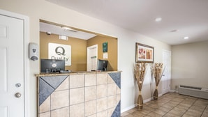 A reception area with a tiled counter, a computer, a sign reading 'Quality,' and two decorative vases. - Quality Inn White Springs Suwanee (White Springs)