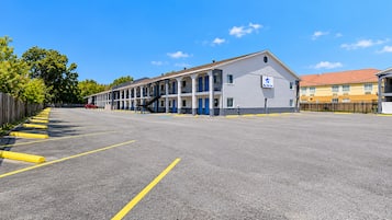 A motel with a row of rooms, a parking lot, and a clear blue sky.