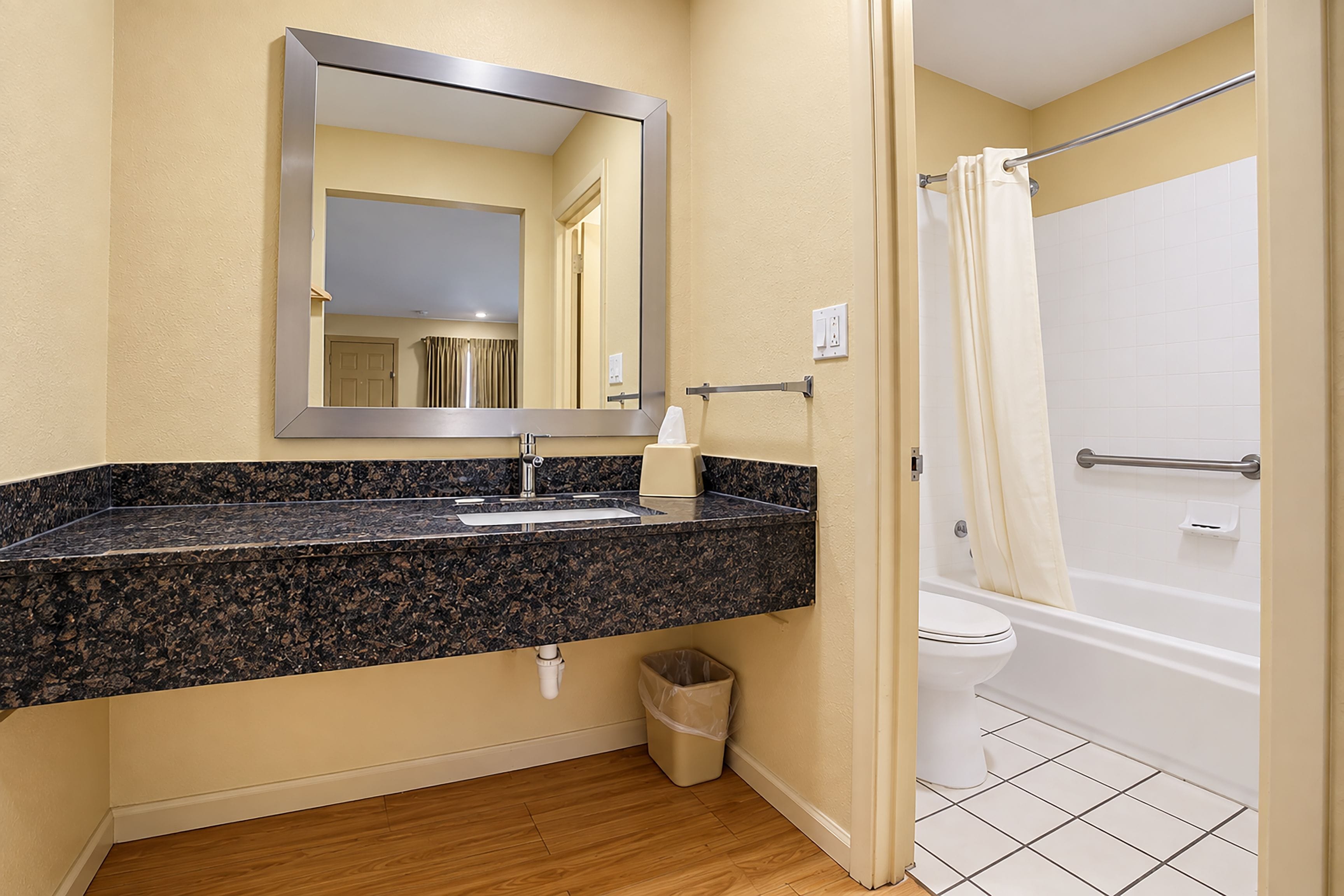 A bathroom with a granite countertop sink, a mirror, a toilet, and a shower with a curtain.