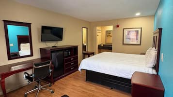A hotel room with a bed, a desk with a chair, a television, a mirror, and a small table.