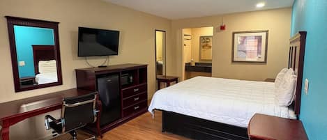 A hotel room with a bed, a desk with a chair, a television, a mirror, and a small table.