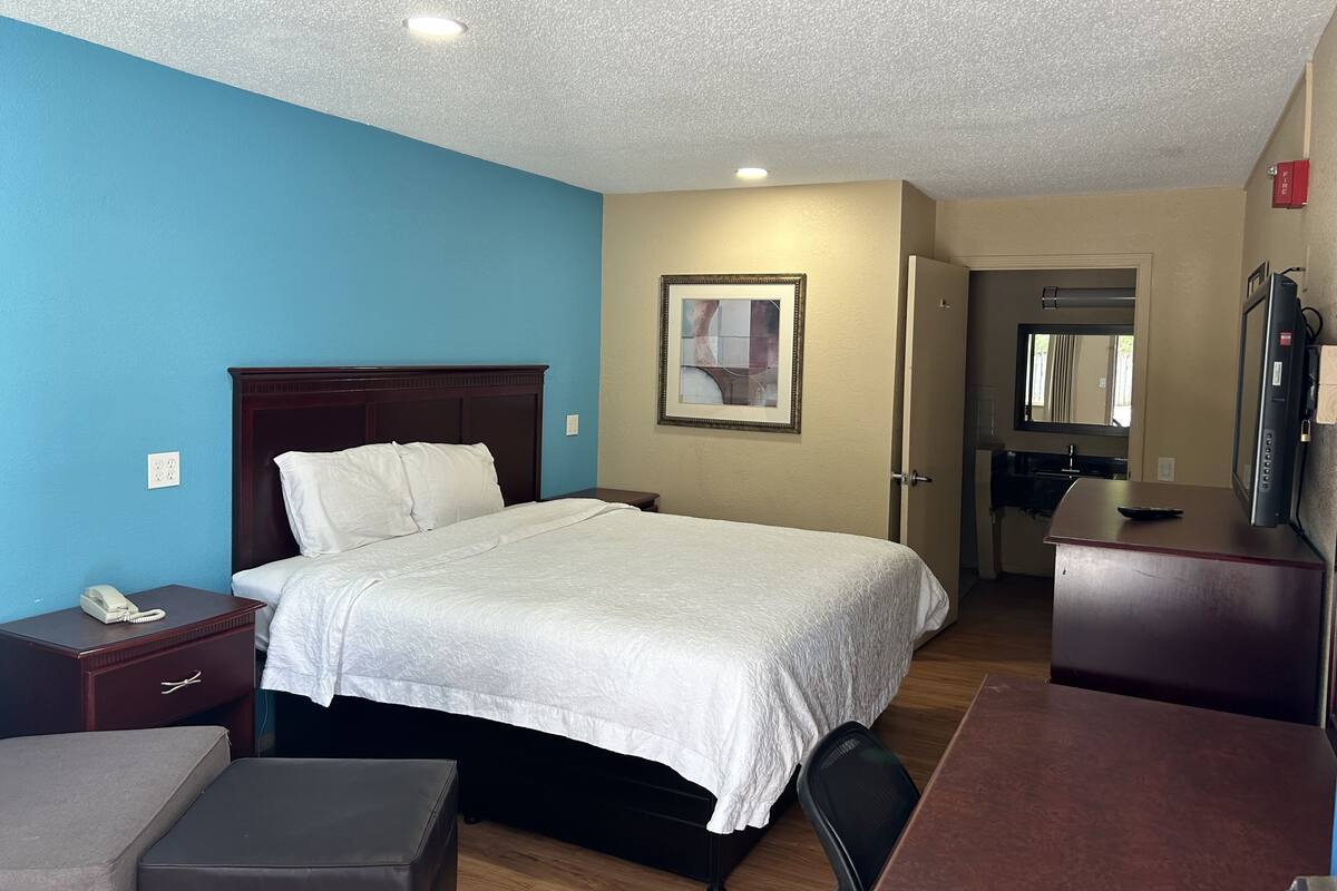 Una habitación de hotel con cama, mesita de noche, silla, escritorio y espejo.