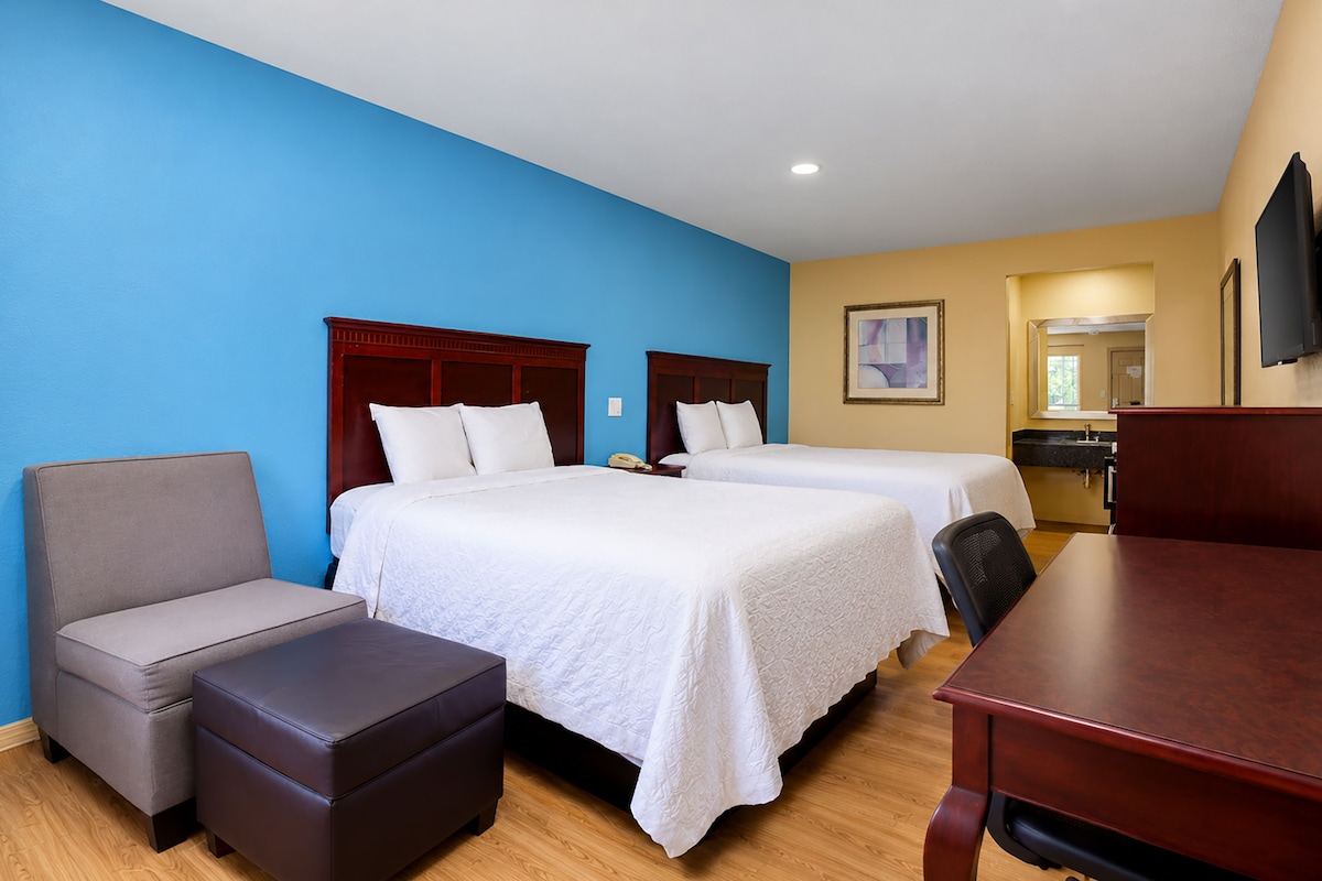 A hotel room with two beds, a desk, a chair, and a small table.