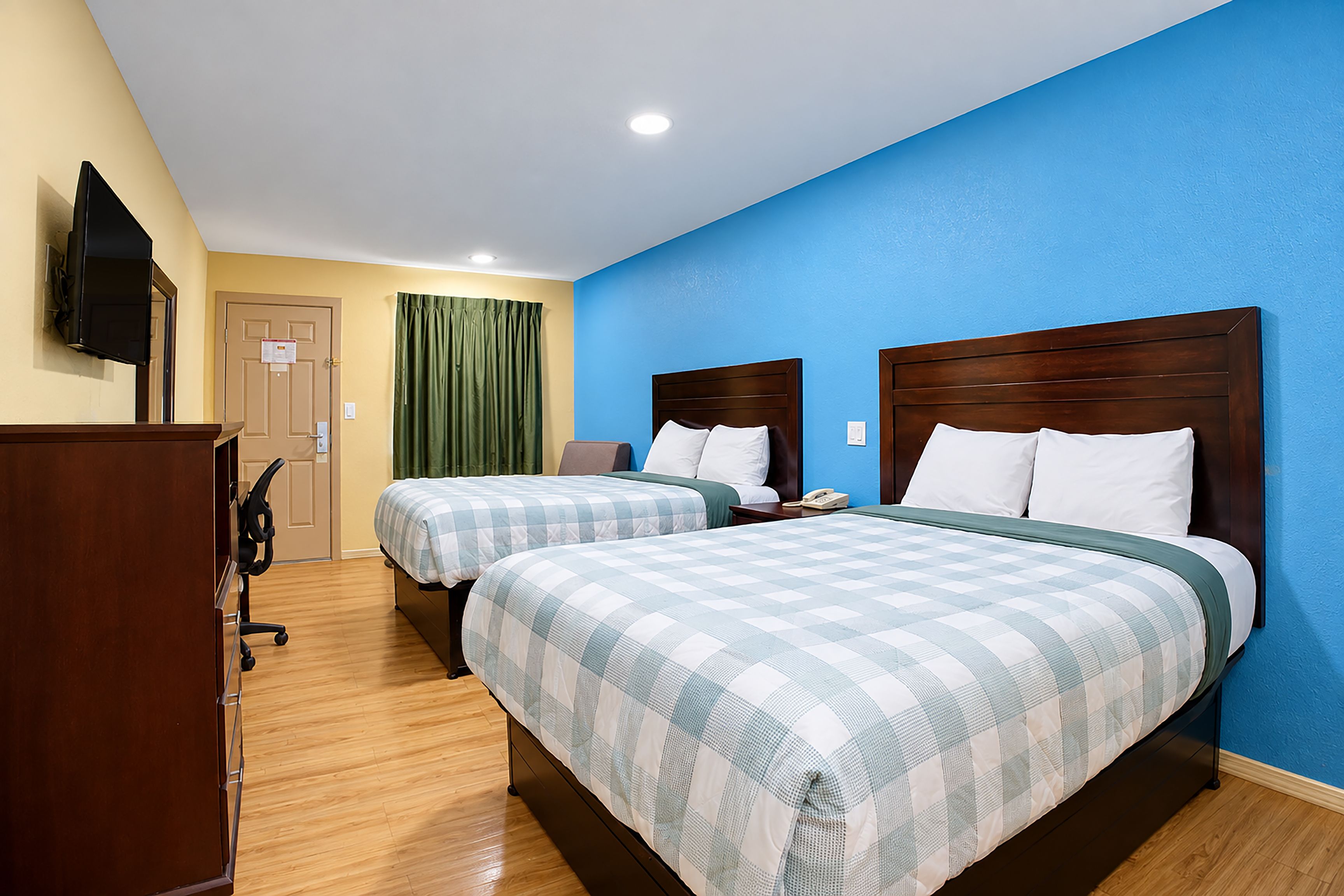 Une chambre d’hôtel avec deux lits, un bureau, une chaise, une télévision et une porte.