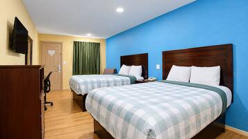 A hotel room with two beds, a desk, a chair, a TV, and a door.