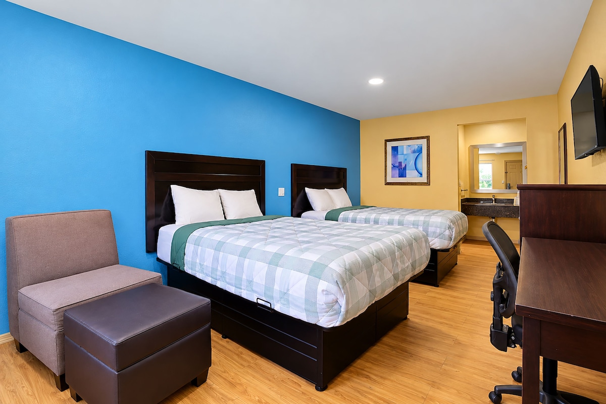 A hotel room with two beds, a desk, a chair, and a TV.