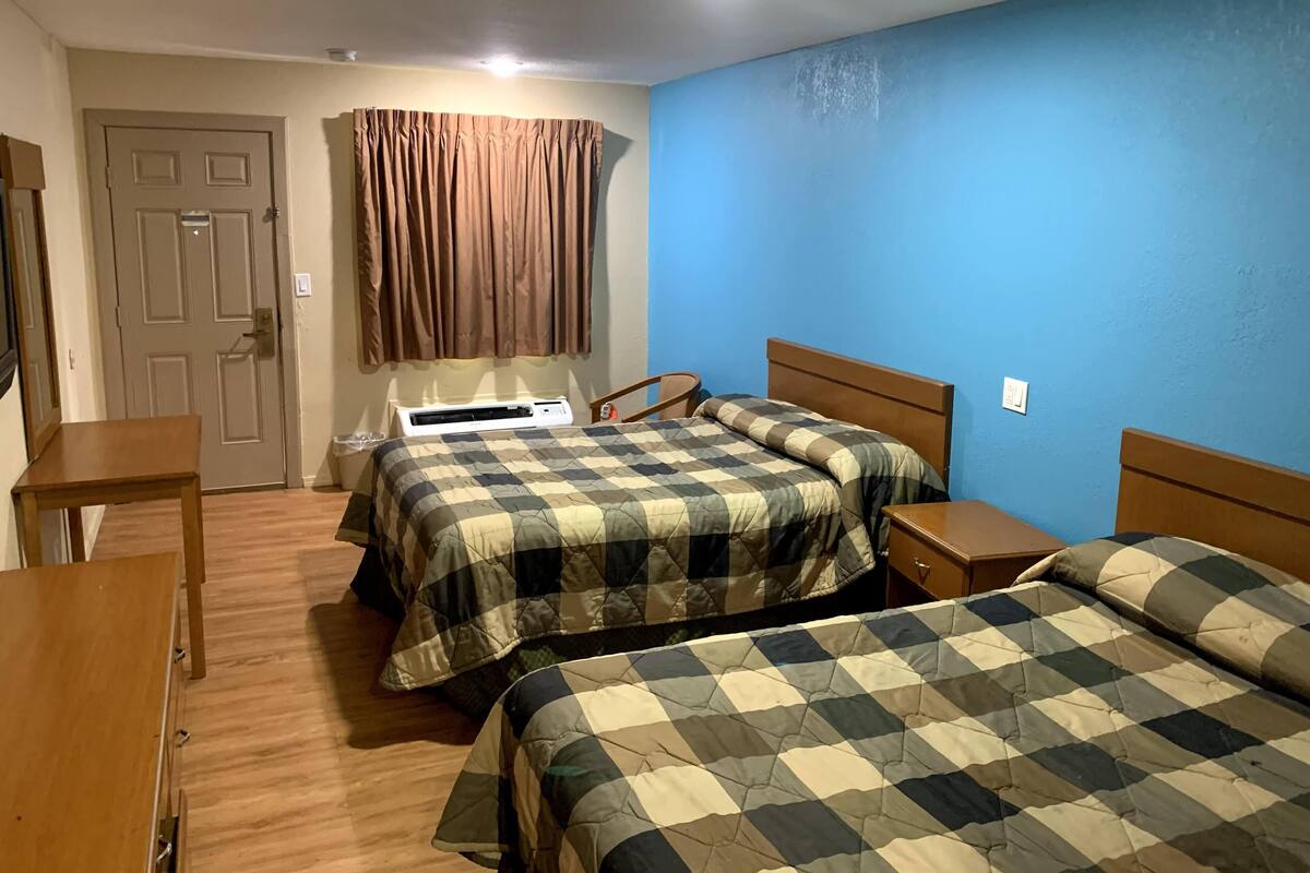 Una habitación con dos camas, un escritorio, una silla, una ventana con cortinas y una lámpara en el techo.