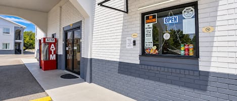 A building with a white brick facade, an ATM, and a window with a 'NO SMOKING' sign.