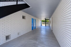 A corridor with white brick walls, a blue door, and a black metal staircase. - Blue Star Inn Lafayette Near Airport I-10 (Lafayette)