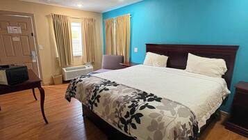 Una habitación de hotel con una cama grande, un escritorio, una silla y un ventanal con cortinas.