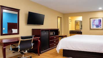 Habitación de hotel con cama, escritorio, silla, televisor, refrigerador y baño con espejo y lavamanos.