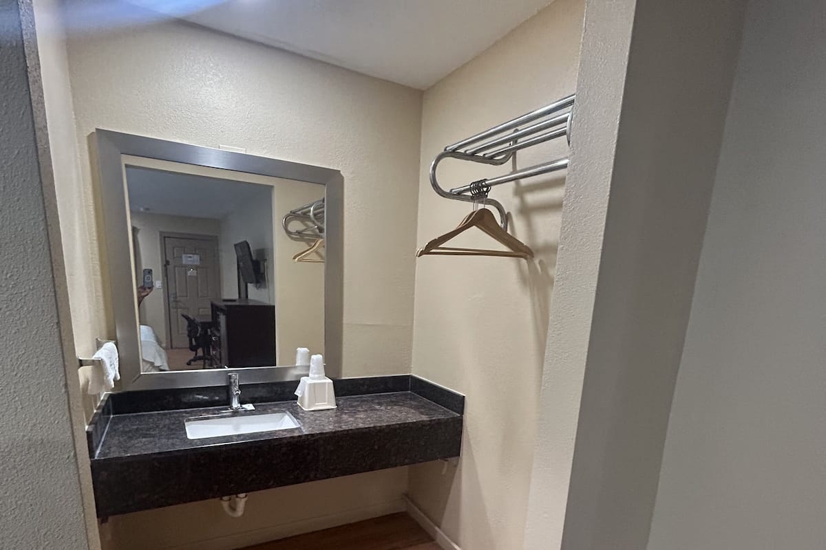 Un baño con lavamanos, espejo, toallero y un banco.